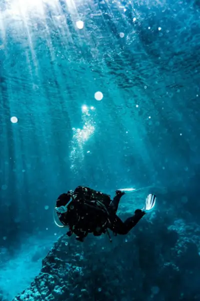 A scuba diver exploring the depths of a clear, blue ocean, surrounded by rays of sunlight filtering through the water. The diver is swimming near a coral reef, creating a serene underwater scene.